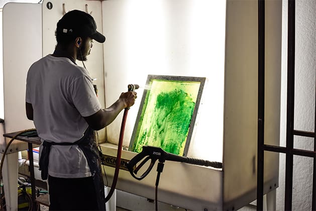 A student washes green paint off of a screen