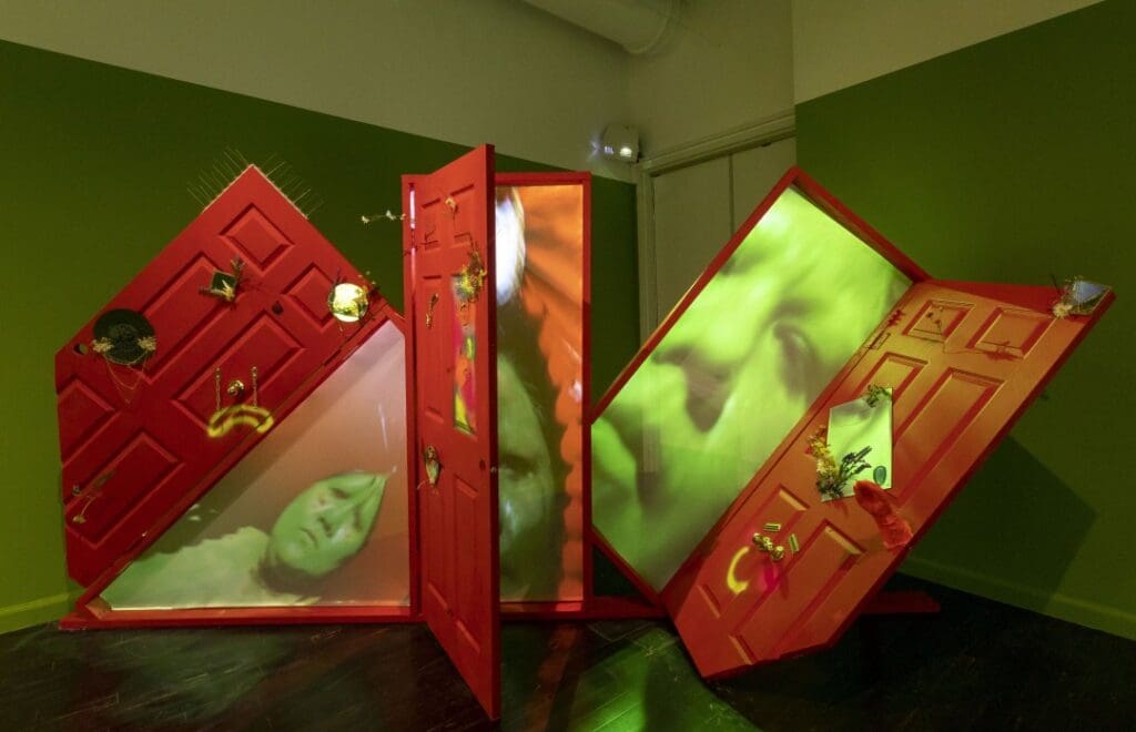 Work by Gabriela Ruiz: a green room with red doors that open to show a green projection of a face
