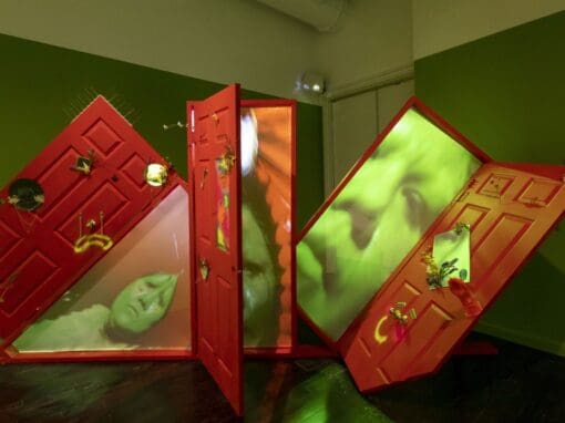 Work by Gabriela Ruiz: a green room with red doors that open to show a green projection of a face