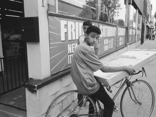 Black and white photo of two boys with a bike and a box leaving a store on the sidewalk
