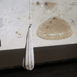 Photo of a exhibition piece. Dirty white cloth hung from ceiling in front of a projection of dirty water droplets on fabric.