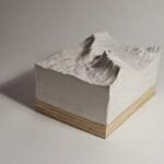 Small ceramic piece of a mountain range mounted onto a wooden board.