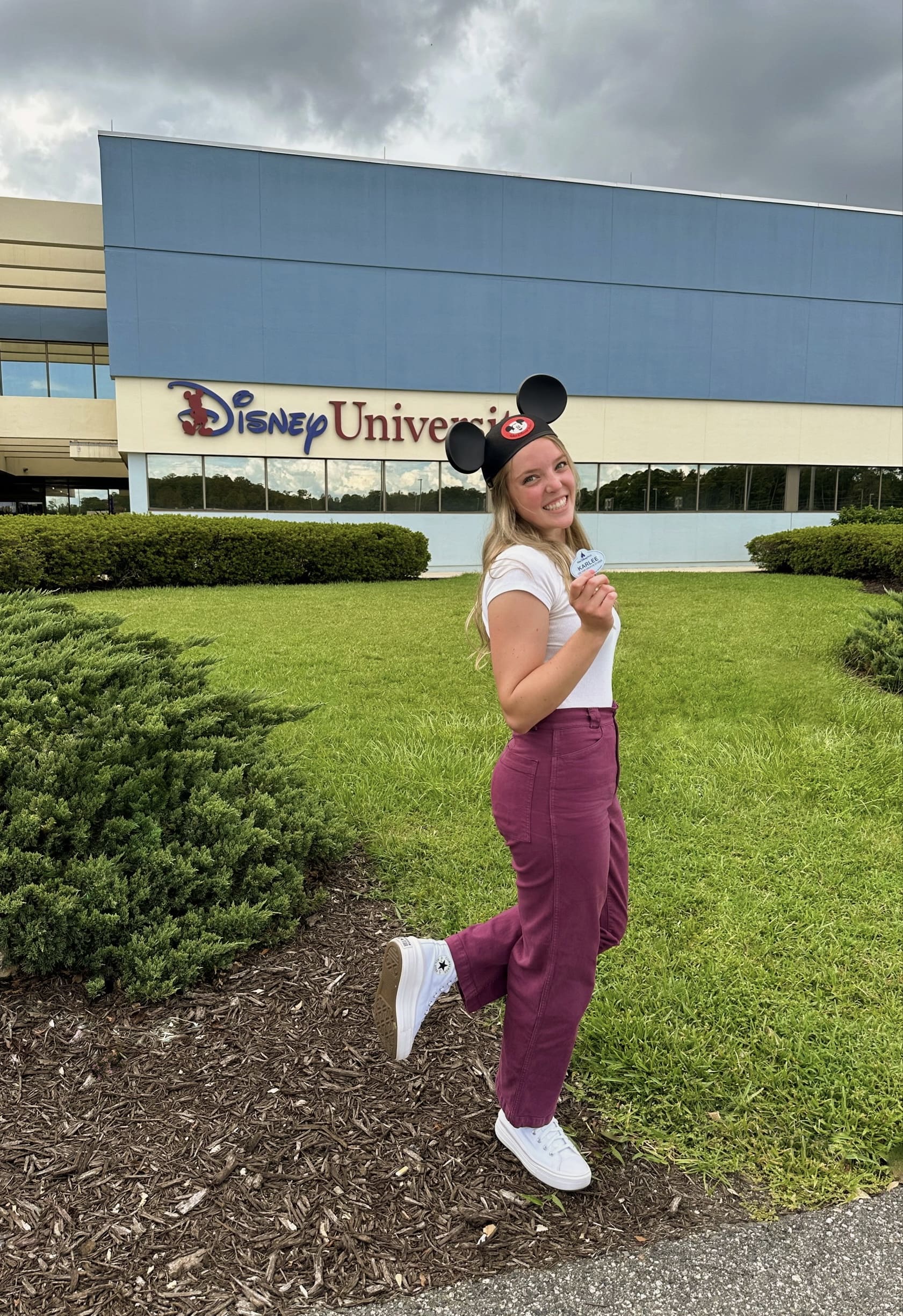 Student with Mickey Mouse ears on head standing outside in front of a Walt Disney University sign.