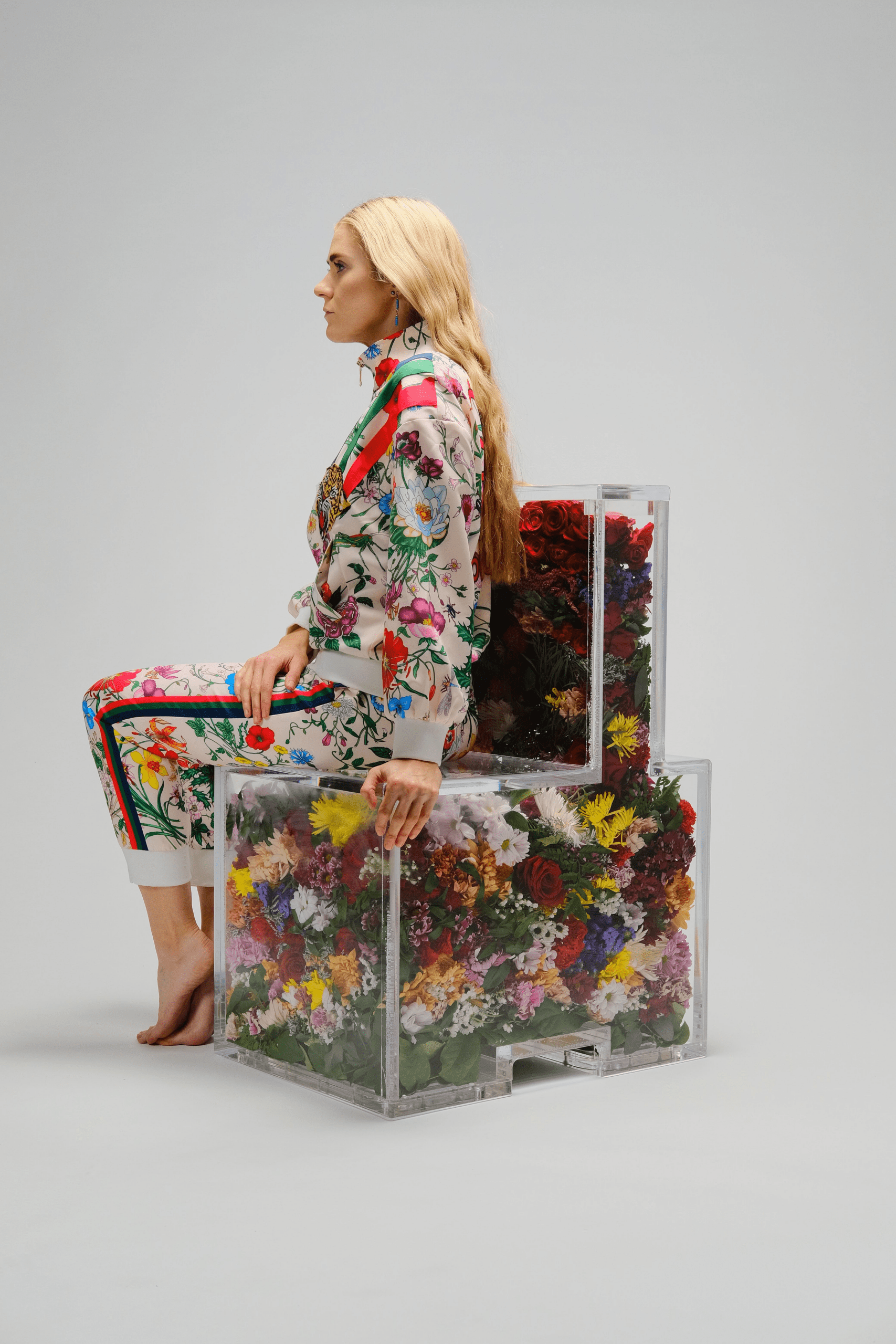 woman in a floral outfit sitting in a transparent chair filled with flowers