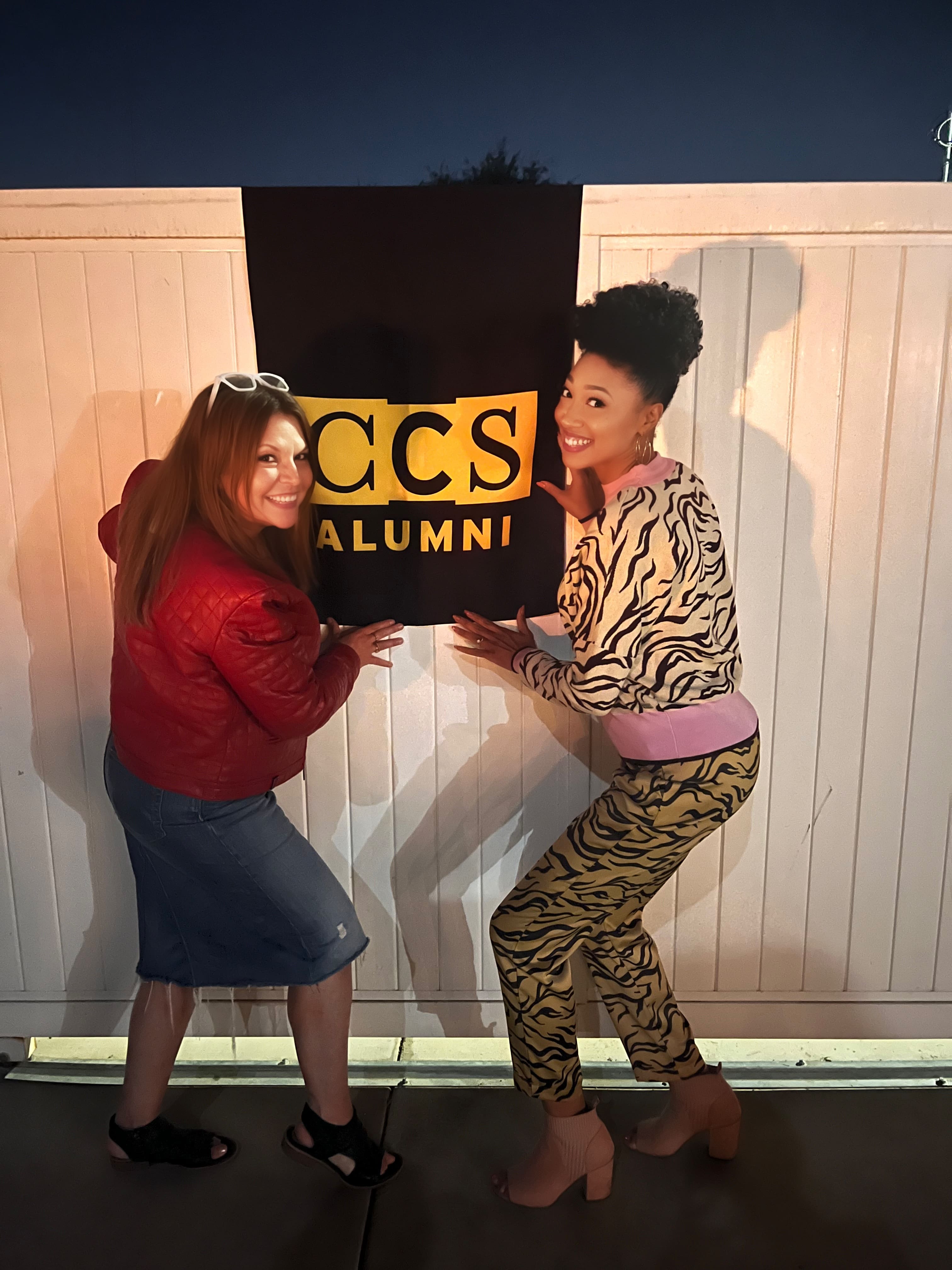 Two alumni standing near the CCS Alumni flag in Burbank