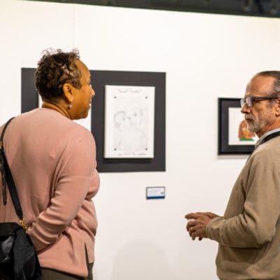 two people talking in front of a wall of artwork at the CAP directors choice exhibition