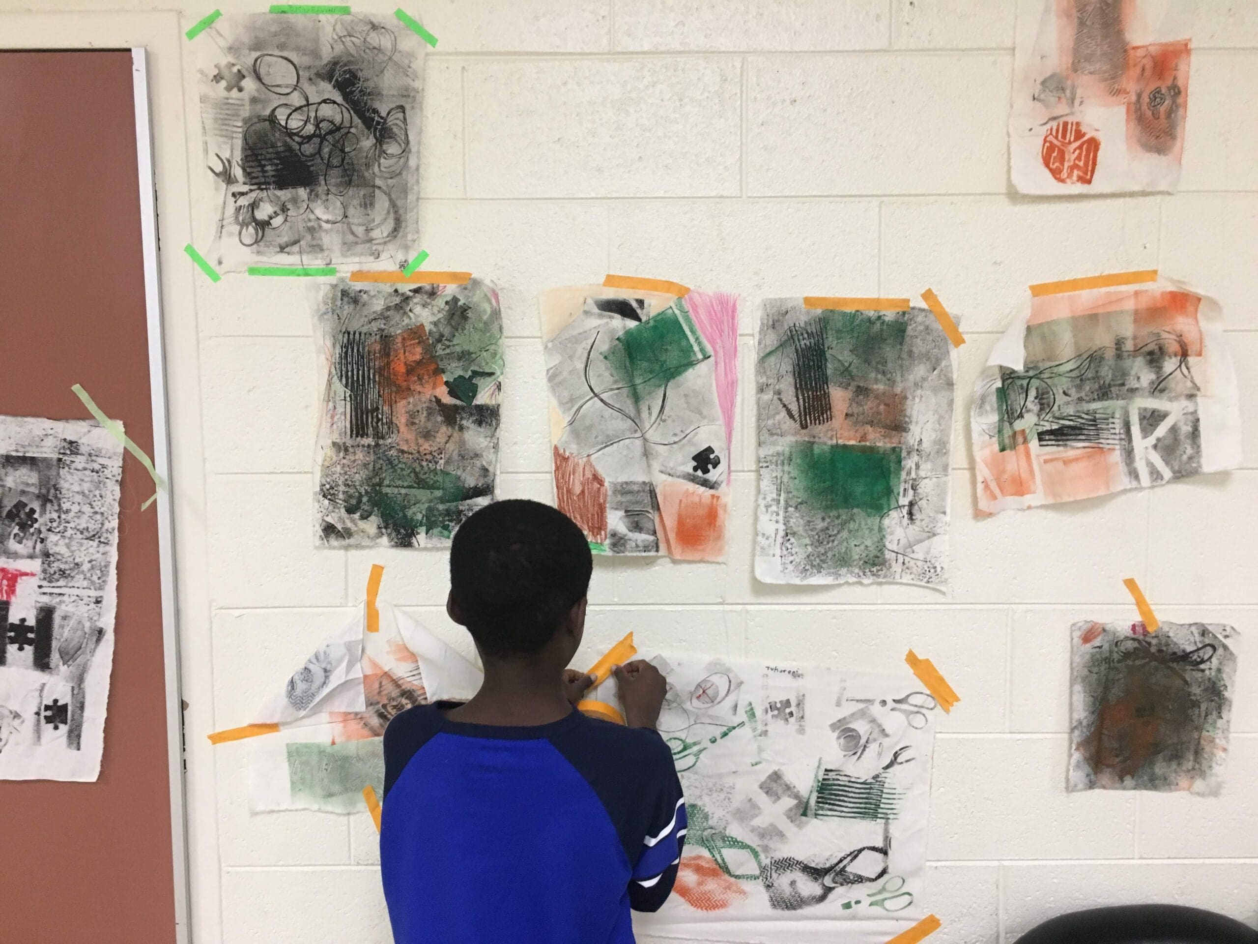 Request a partnership (1) student taping artwork to the wall