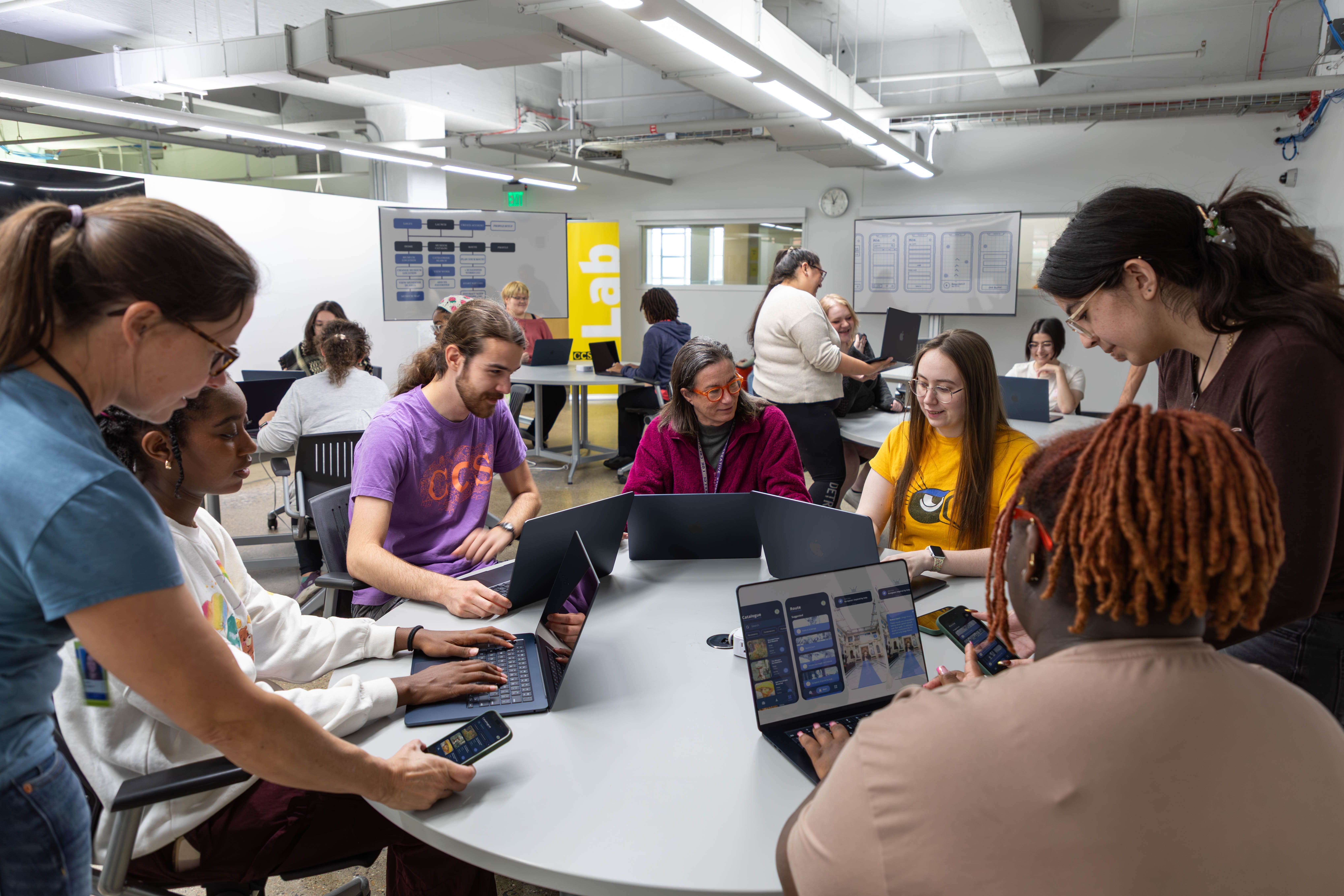 Students gather around a round table, working collaboratively on app design and development using laptops and smartphones as part of CCS's Apple Foundation Program.