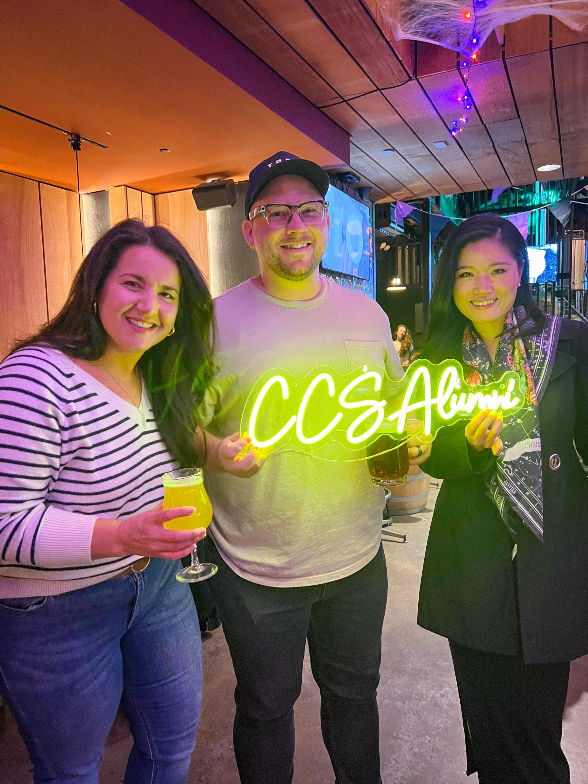 Three alumni at the Brooklyn NY alumni reception holding a neon CCS alumni sign