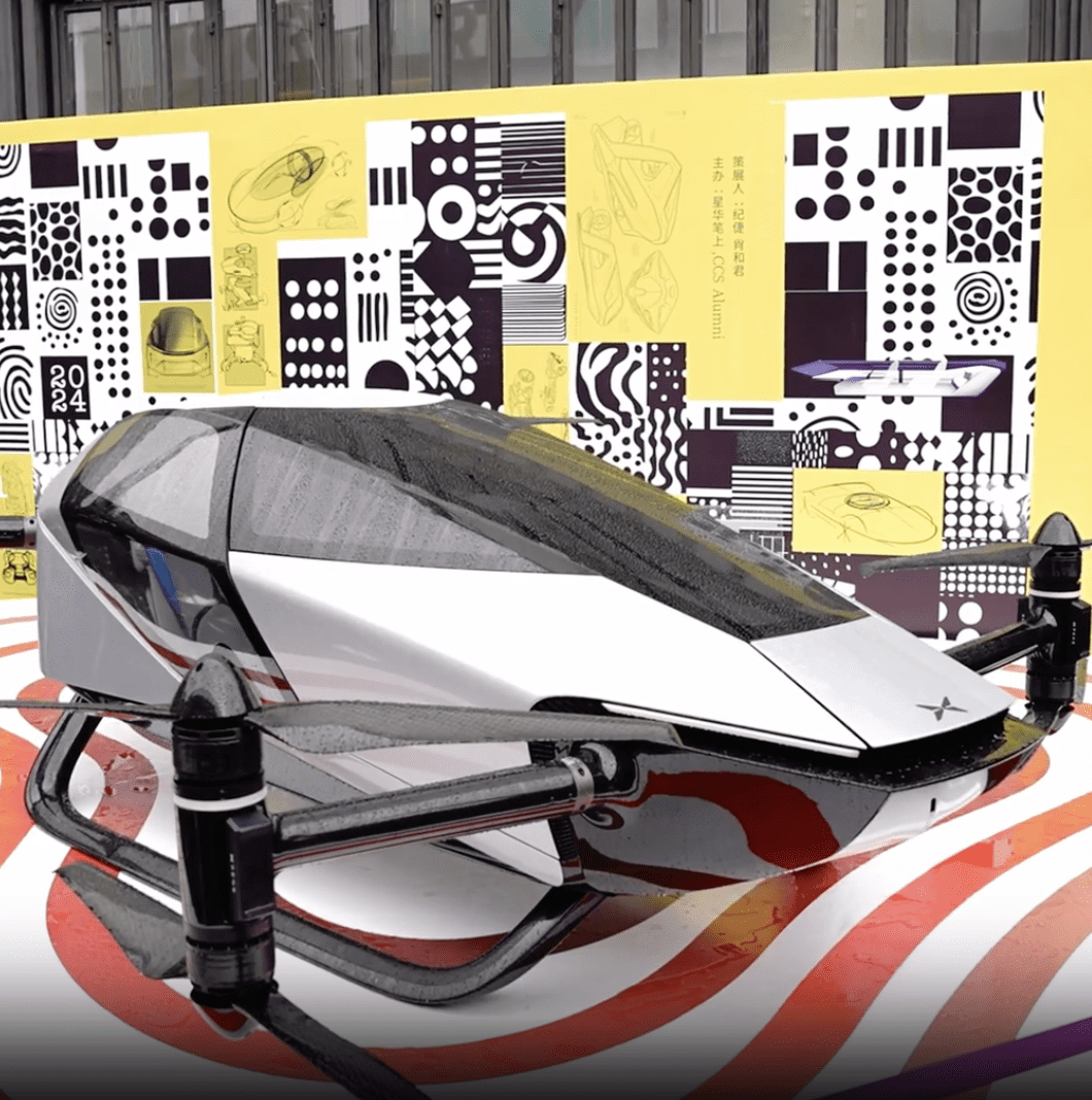 Futuristic black and white vehicle on display in front of a patterned mural featuring geometric patterns, as part of a design exhibition.