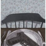 A handgun resting on a decorative plate at a dining table, with a knife and fork on either side. A dark chair is pulled up to the table, set against a background of light blue floral wallpaper.