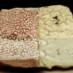 A close-up of a textured art piece. The square piece is divided into four sections with different surface textures and colors: top left is a reddish-brown with a bumpy texture; bottom left is a tan color with a white, coral-like texture; top right is a cracked yellow-green glaze; and bottom right is a smoother, light green glaze.