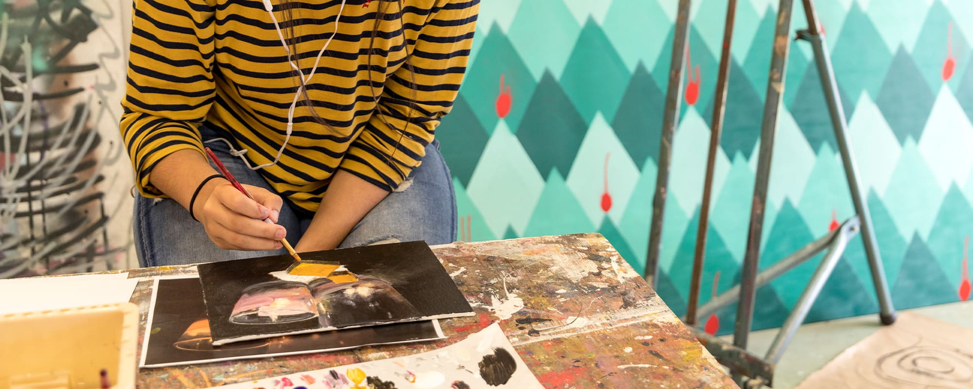 An overhead shot of a CCS student with headphones in painting at a desk.