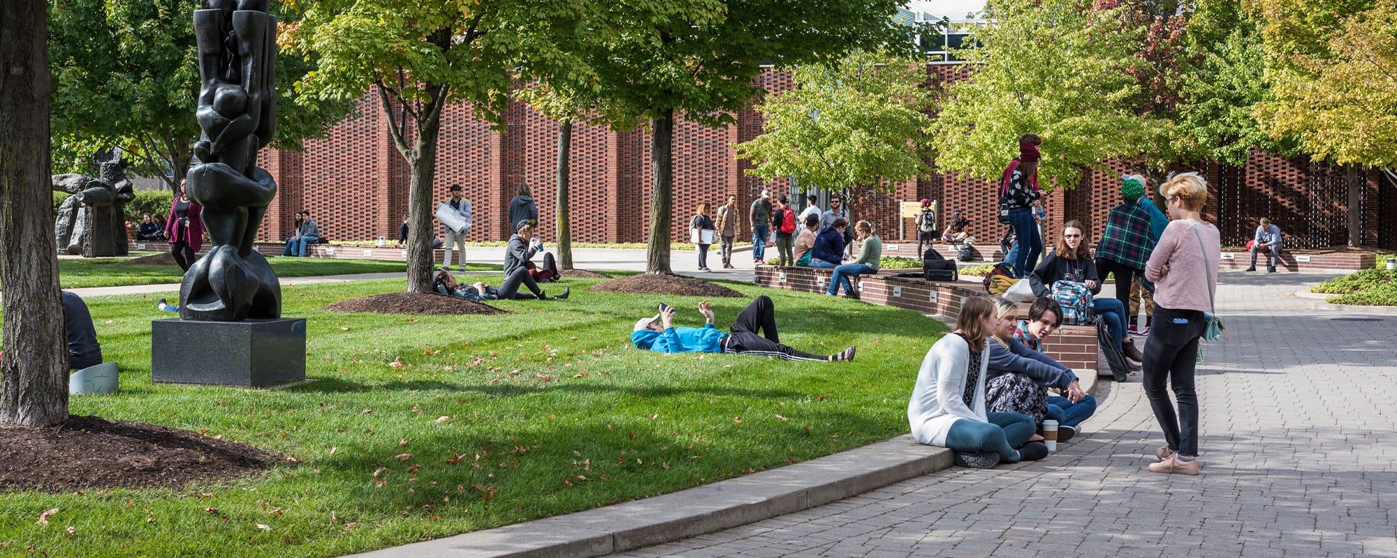 Students walk on the College for Creative Studies campus amongst statues and trees.