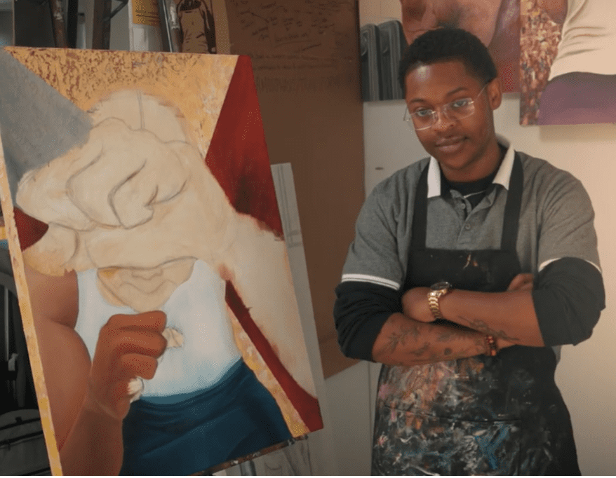 Neo Hopkins standing with his arms crossed in front of his painting