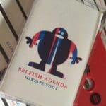 A "Selfish Agenda Mixtape Vol 1" cassette tape featuring a blue and red character illustration.