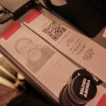Printed receipts displaying an ASCII portrait and QR code taped next to "Selfish Agenda" stickers.