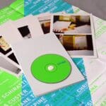 A "SPINE" CD in a clear sleeve sitting atop a green and white folded poster featuring names and photos.