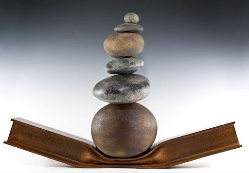 "Harris - 1983, From The Awakening of Harris Wolf" Black-and-white photograph by Glenn Triest of a lively street scene featuring individuals dressed in elaborate costumes for a parade or festival. The central figure wears a feathered mask, a leather vest, and multiple bead necklaces. To his right, a man in a curly wig and sparkling outfit gazes directly at the camera, holding a drink. Other participants in festive attire and masks fill the background.