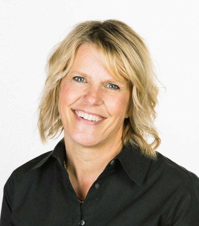 Professional studio portrait of Allison J. Puff, a woman with shoulder-length wavy blonde hair and blue eyes, smiling warmly. She is wearing a black collared button-down shirt against a plain white background.