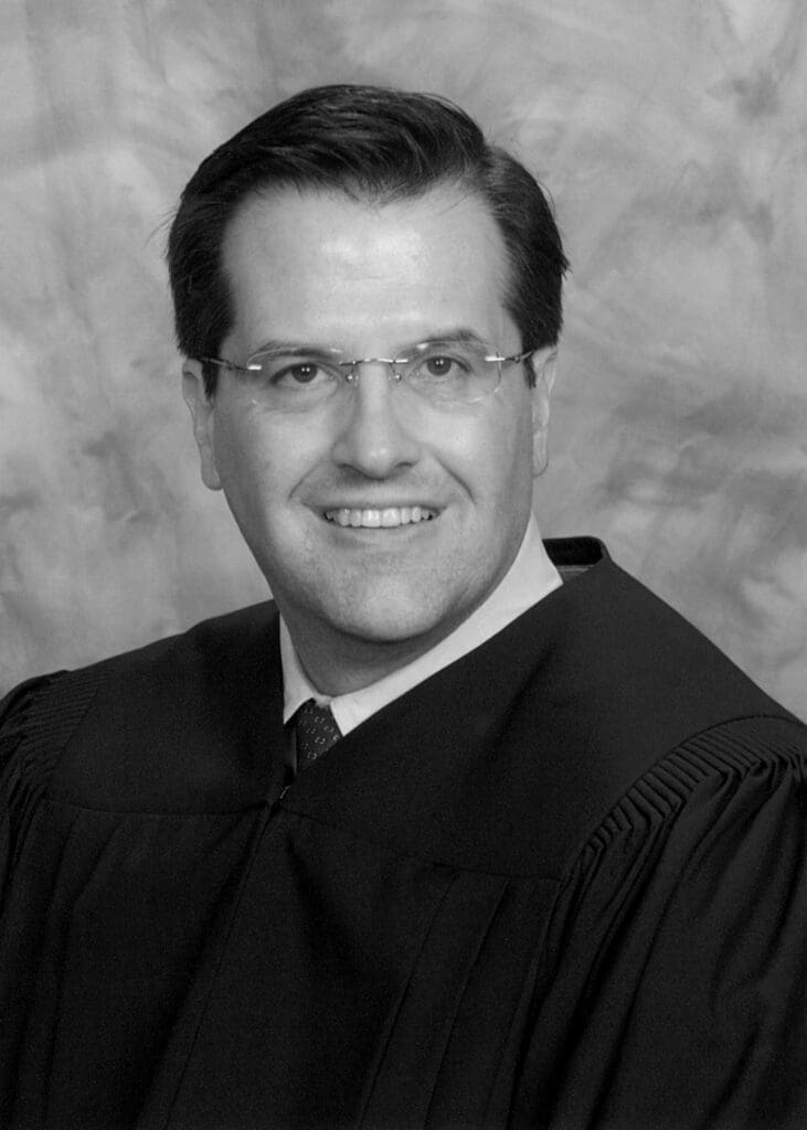Black and white headshot of Judge Stephen J. Murphy III in judicial robes and rimless glasses, smiling.