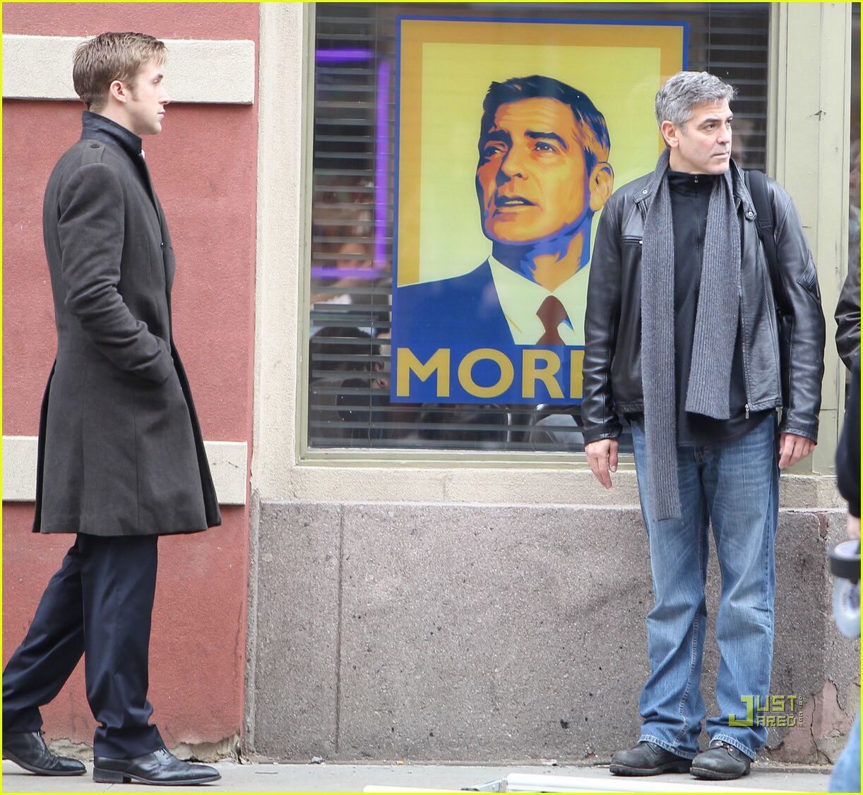 JPEG image 2 A medium shot of Ryan Gosling as Stephen Meyers in "The Ides of March," standing stoically in a crowded campaign rally. Behind him, supporters hold various political prop posters designed by Michael Maher Jr., featuring George Clooney's character, Mike Morris, with slogans like "Believe" and "I Like Mike."
