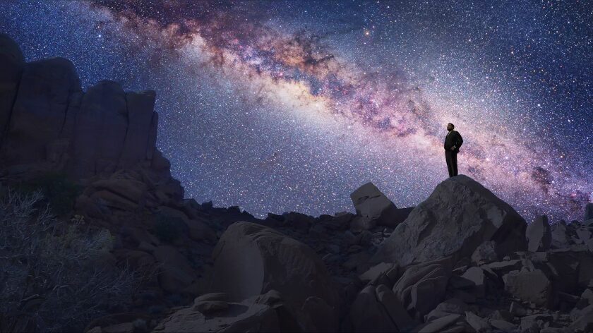 Stills of Michael Maher's work in Cosmos A man in a suit stands on a rocky desert peak, looking up at a brilliant, detailed view of the Milky Way galaxy stretching across the night sky. This cinematic still highlights Michael Maher’s visual effects work for the television series Cosmos.