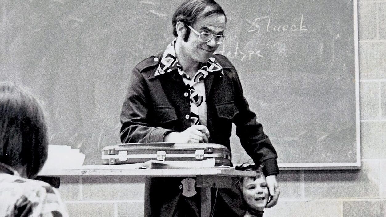 Professor James S. Goldwasser with his young son at the College for Creative Studies (CCS) in the 1970s. This candid black-and-white photography student's snapshot captures a heartwarming moment during a design lecture, featuring the professor at a drafting table and his laughing child.