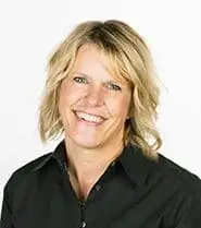 Professional studio portrait of Allison J. Puff, a woman with shoulder-length wavy blonde hair and blue eyes, smiling warmly. She is wearing a black collared button-down shirt against a plain white background.