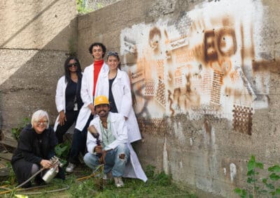 A group of students, faculty, and an industry partner posing in front of a mural created with bio-based sustainable spray paint created by the students at the College for Creative Studies