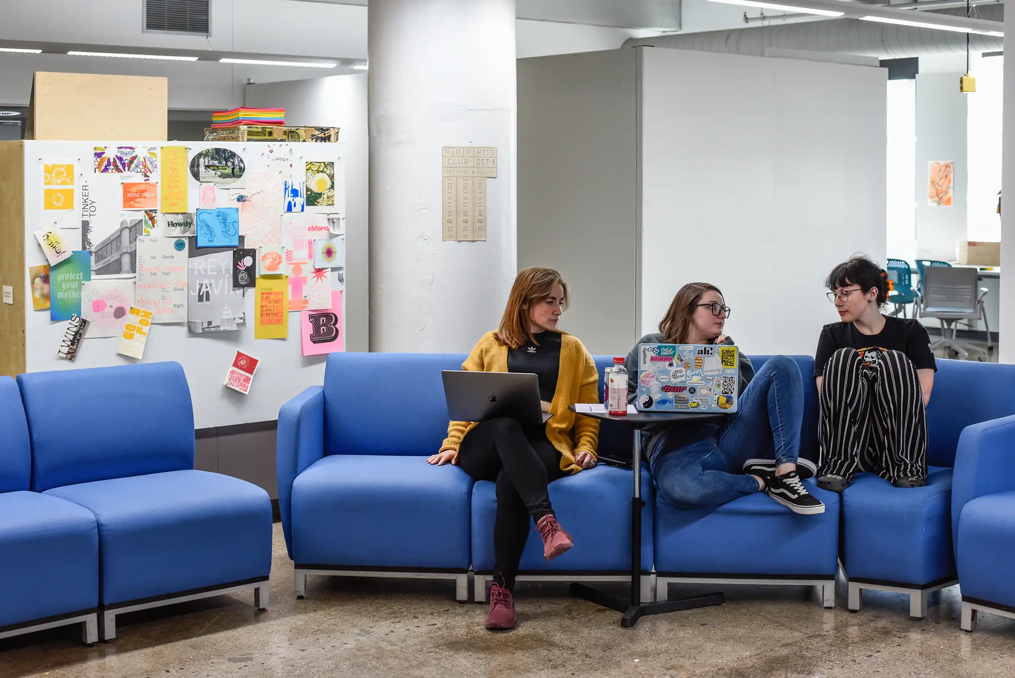A group of students on a blue couch, gathered around a laptop on a small table