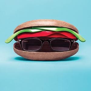 Advertising Design. A pair of black glasses inside a burger, between the bun and tomato, on a blue background.