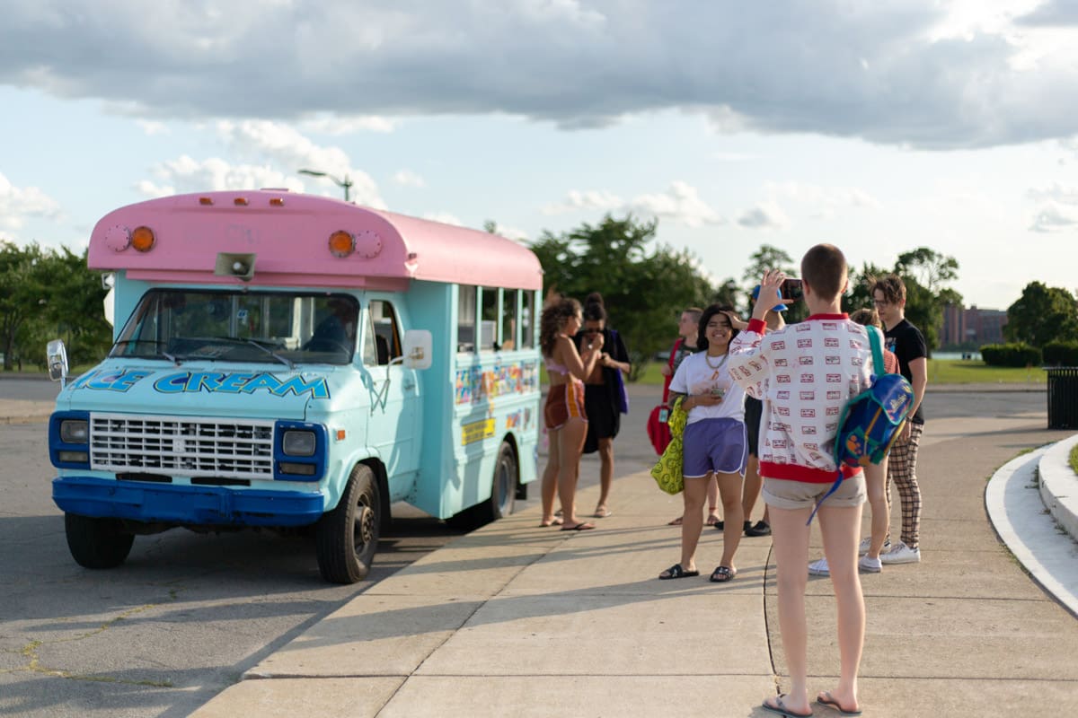 Photo of a group of students standing outside a brightly colored blue bus with a pink roof