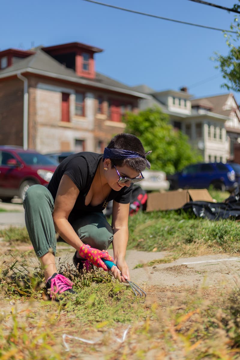 A smiling student pulling weeds out from a public sidewalk as an act of community service