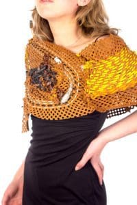 Photo of a model's torso wearing a black dress and a cowl made out of dark orange perforated fabric with various types of cord and string interwoven through the holes.