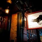 Photo of a sign outside of a shop at night. The sign is of a black crow on white wood with a red frame