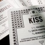 A stack of black and white cocktail menu cards on a wooden table
