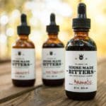 Three dropper bottles of Housemade Bitters- Small Batch Cocktail Flavoring on a wooden table