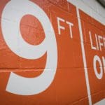 Orange sign painted on a white brick wall that says "Nine feet- lifeguard on duty"