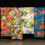 Four brightly colored floral printed fabrics hanging off of a T-stand
