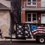 Photo of a man walking down a neighborhood street. On the road is a trailer painted with the Union Jack flag.