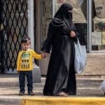 Photo of two women wearing black niqabs and a little boy waiting at a crosswalk.