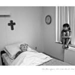 Black and white photo of a young girl sitting on the window sill of a hospital room, looking at a sickly elderly woman sleeping in a hospital bed.