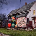 Photo of a house painted with a mural of three vase bouquets and text that says "This is a Home, do not bid!"