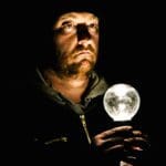 High contrast photo of a serious looking man holding an illuminated white lightbulb close to his chest