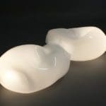 Sculpture on a black backdrop comprised of two white semi-ovular lamps