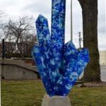 Blue sculpture of tall crystal points speckled with white, jutting out of a cement base.