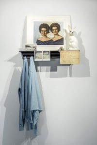 shelve of photos, a ceramic bunny and 2 jean shirts hanging off of it