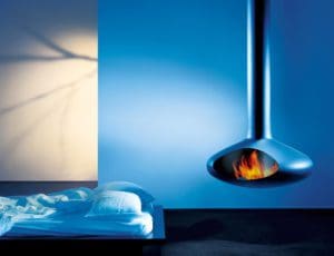 an unmade bed next to a metal fireplace