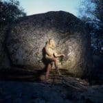 a figure leaning against a rock with one foot on a bike